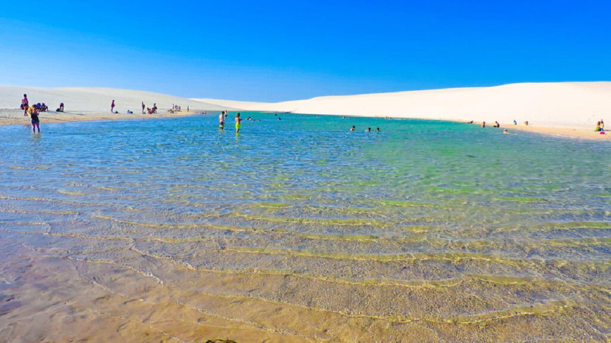 Pessoas brincando e nadando nas lagoas sazonais de águas cristalinas entre as dunas brancas dos Lençóis Maranhenses